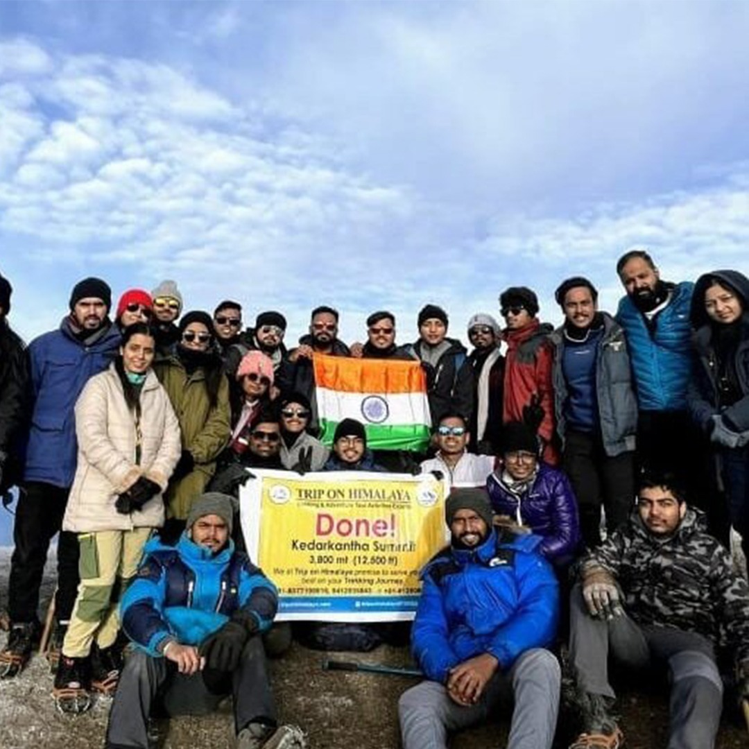 Group of trekkers holding flags at Kedarkantha Summit after a successful climb