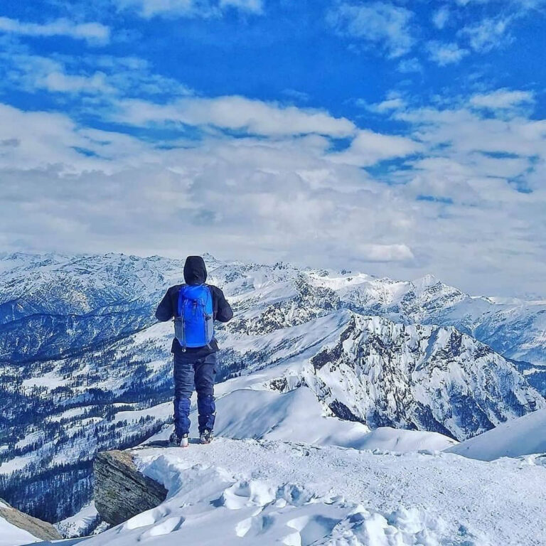 Panoramic view from the Kedarkantha Summit with clear blue skies and snow-capped mountains.