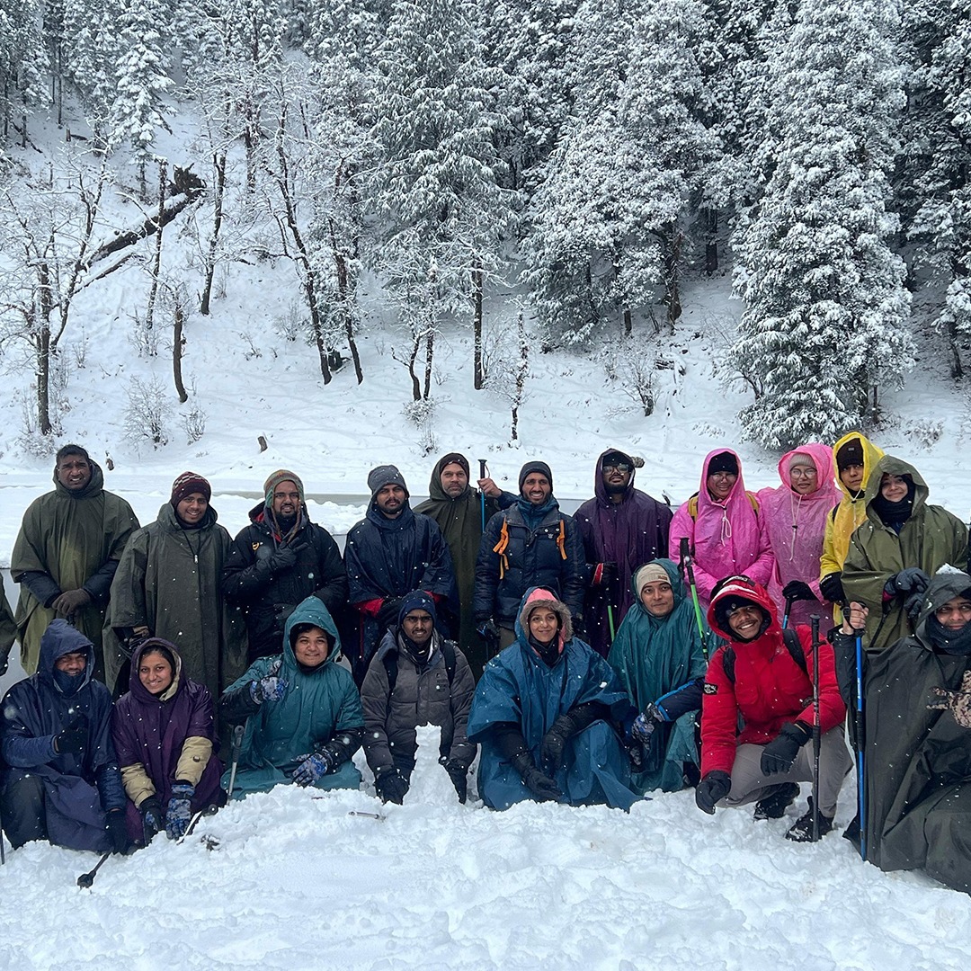 Group of trekkers at Juda Ka Talab with a scenic frozen lake and pine forest backdrop