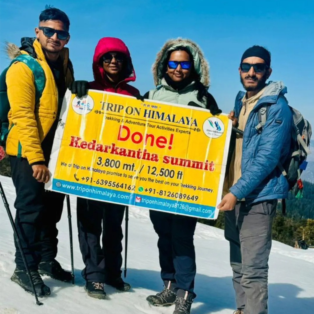 TripOnHimalaya banner at Kedarkantha Summit with a breathtaking view of snow-covered Himalayan peaks